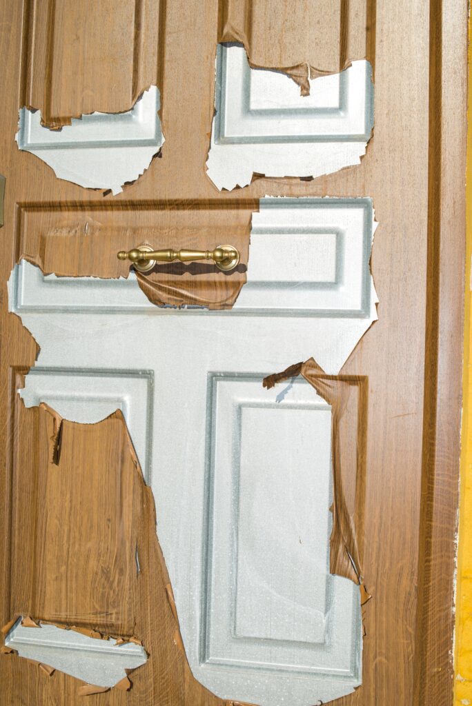 Close-up of a severely damaged wooden door with peeling paint, highlighting deterioration.