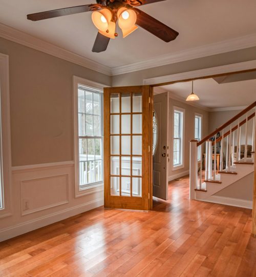 Spacious living room with wooden French doors and ceiling fan, showcasing contemporary interior design.